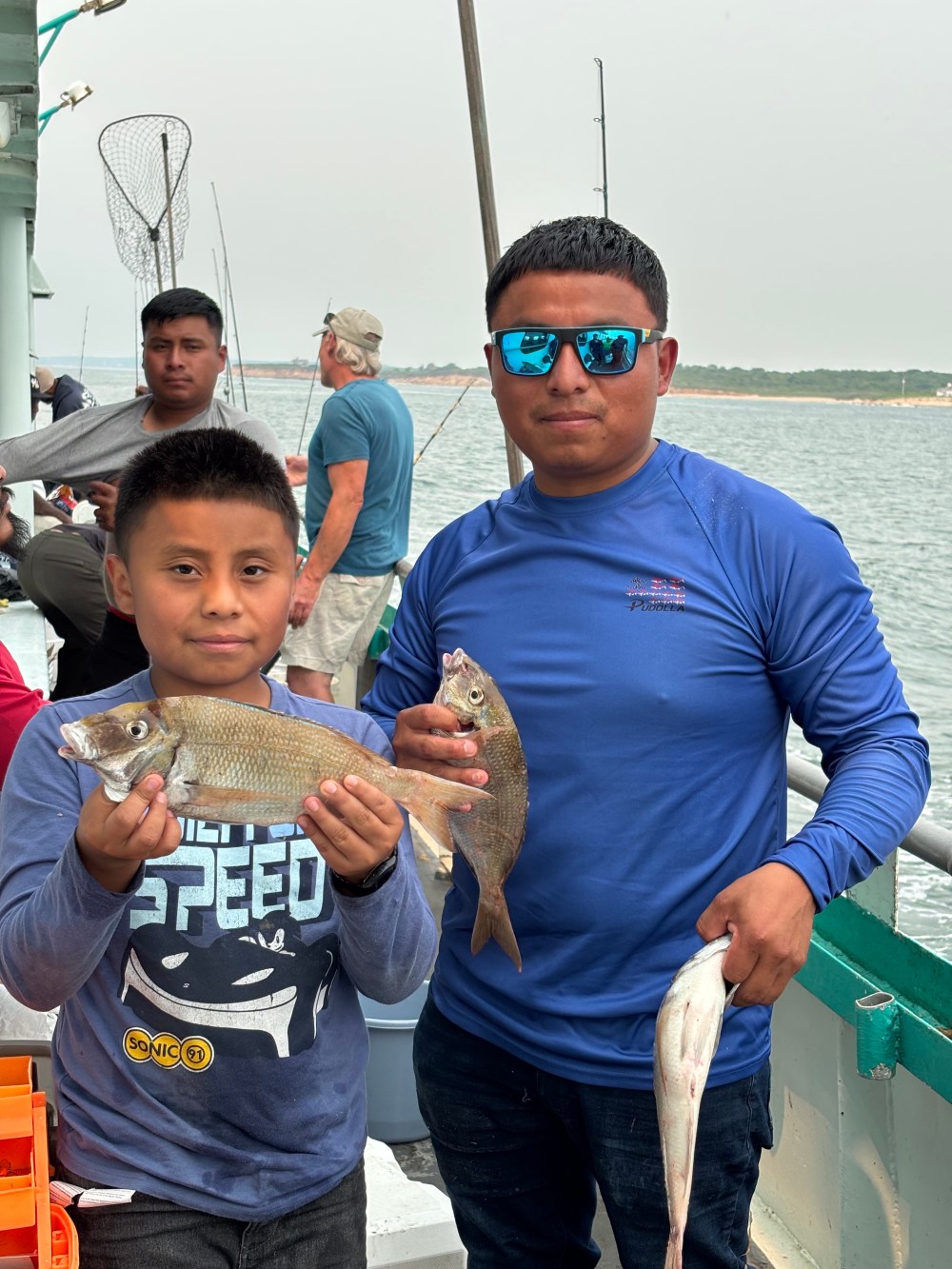 Two people holding fish on a boat with fishing gear visible.