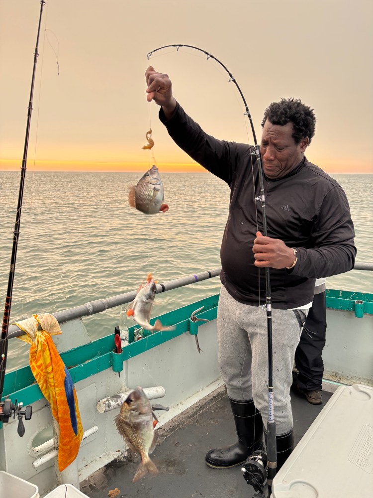 Person holding fishing rod with three fish, standing on a boat at sunset.