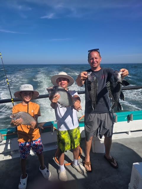 Three people on a boat holding fish, with ocean in the background.