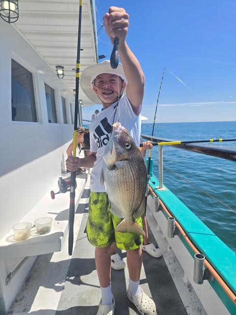 Person holding a fish on a boat, wearing a hat and shorts, with fishing rod.