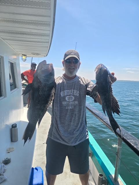 Man holding two fish on a boat, ocean in background, sunny day.