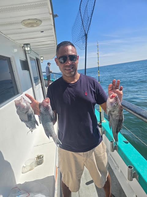 Man on boat holding three fish with ocean background.