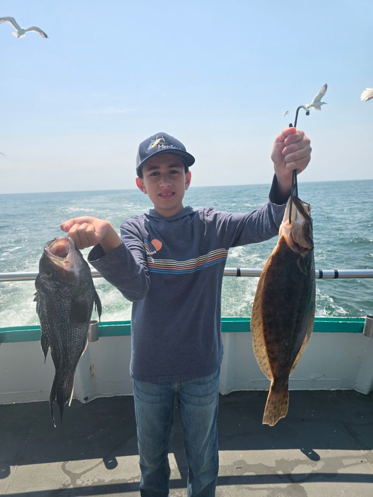 Boy on boat holding two fish with ocean in background