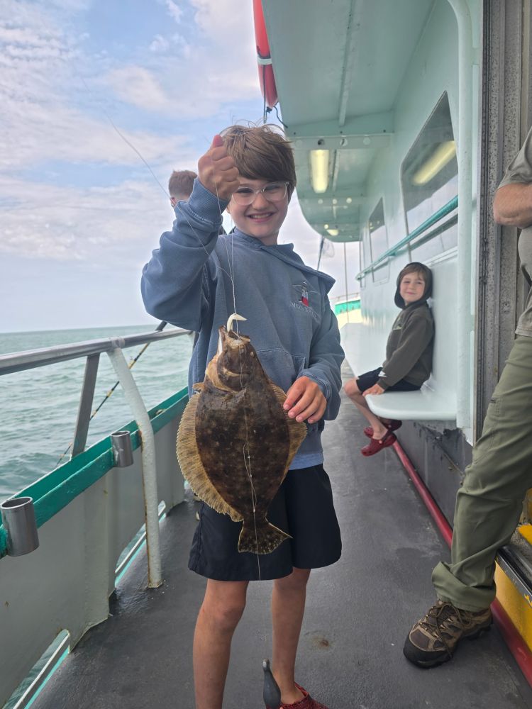 Child holding a fish on a boat with another child seated in the background.