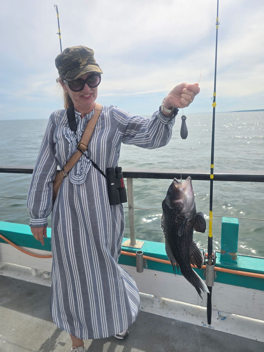 Person in striped dress on boat holding a fish with fishing pole.