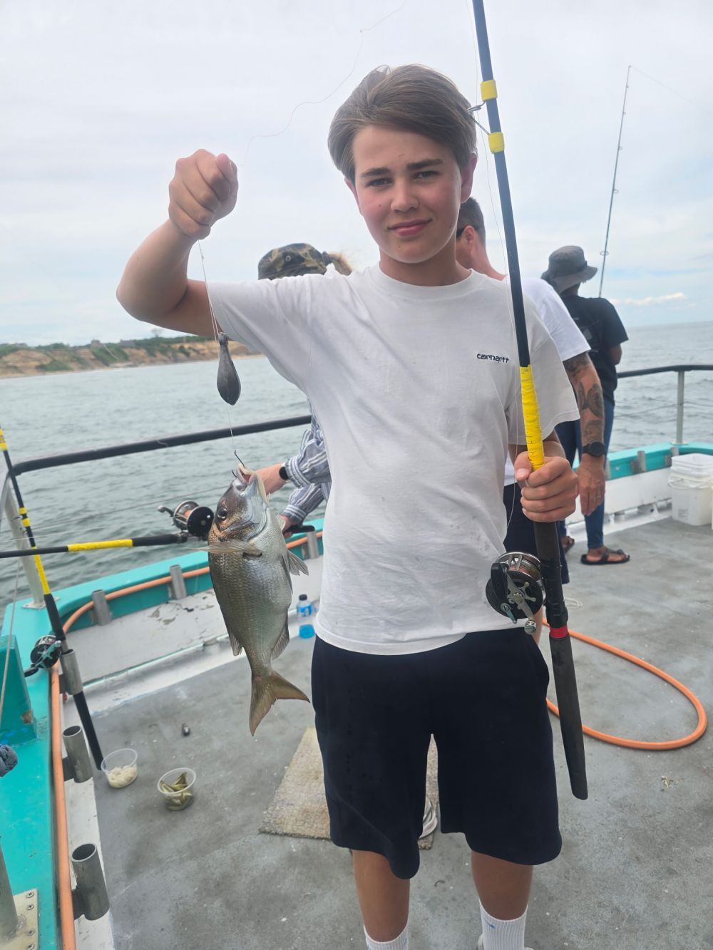 Young person holding a fishing rod with a fish on a boat.