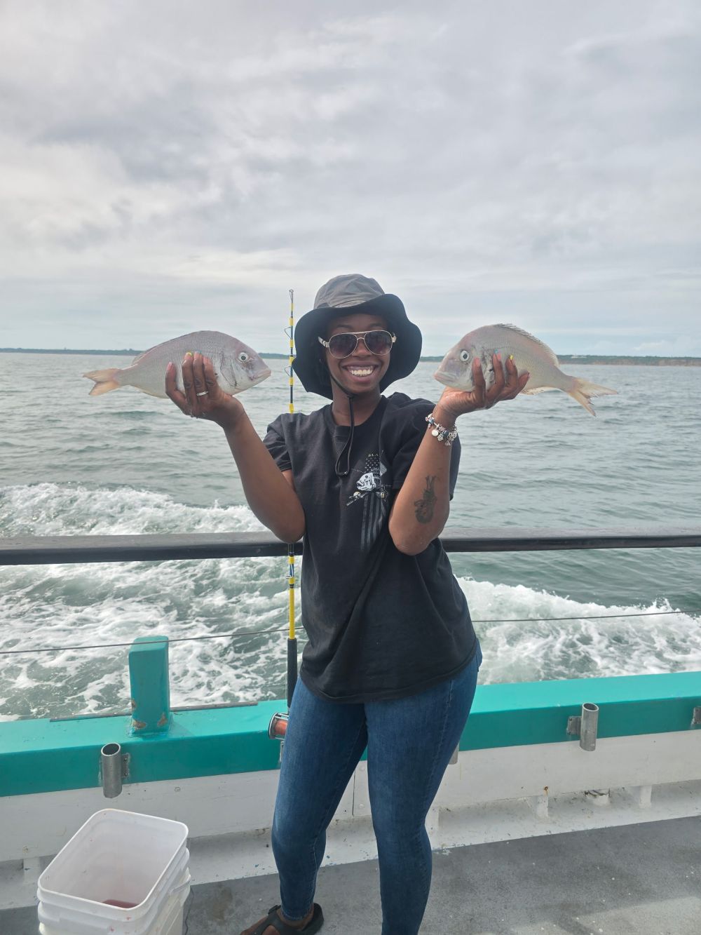 Person on a boat holding two fish, smiling, with ocean in the background.