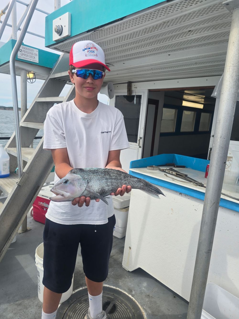Person holding a fish on a boat deck, wearing a white t-shirt and cap.