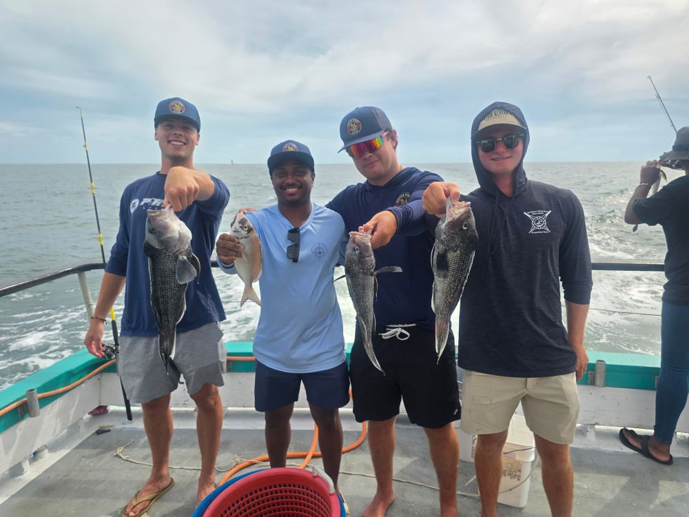Four men on a boat holding up fish they caught.