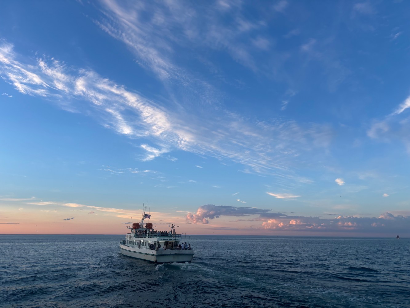 Ferry on the ocean under a sky with scattered clouds at sunset.