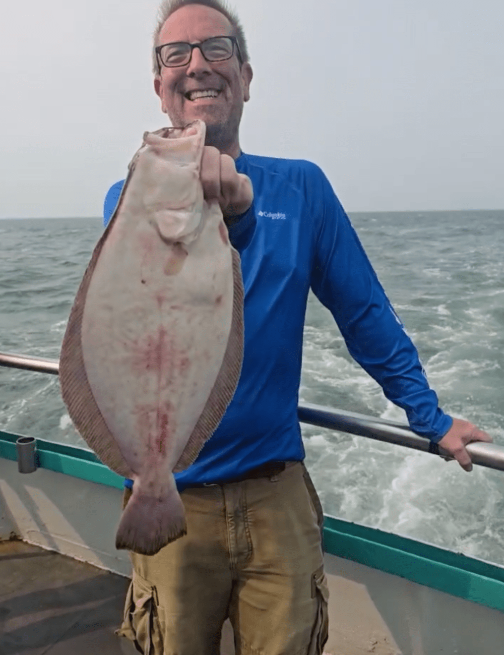 Man in blue shirt holding a large fish on a boat at sea.