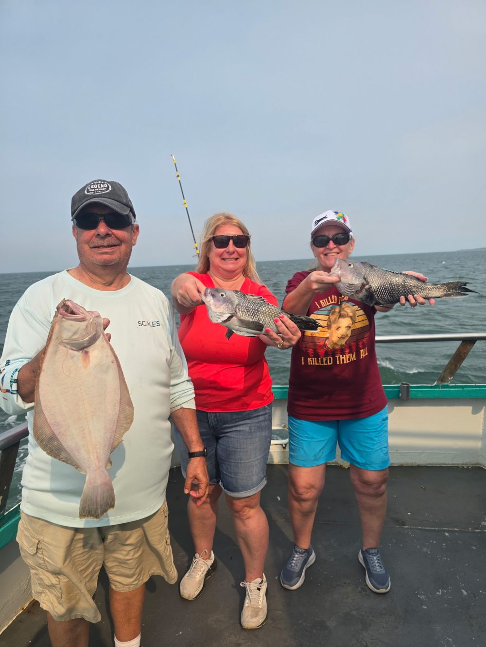 Three people on a boat holding fish with smiles.