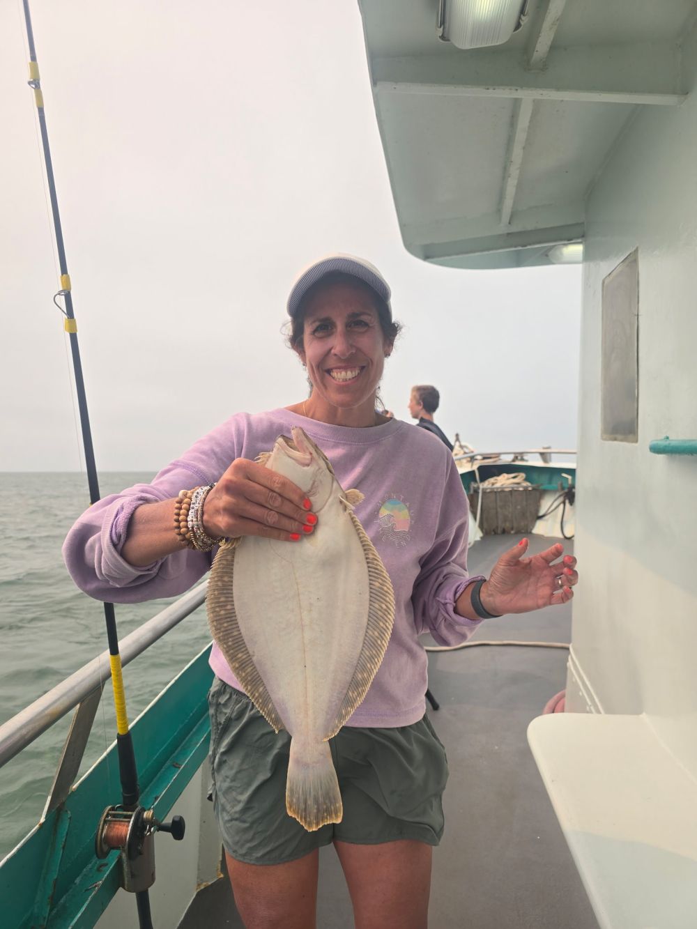 Person on a boat holding a flat fish, smiling at the camera.
