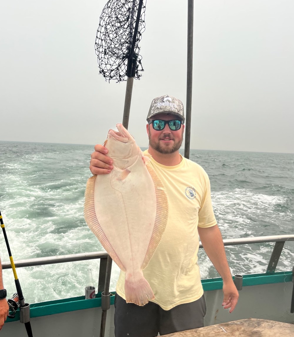 Man on boat holding a large fish with ocean in the background.