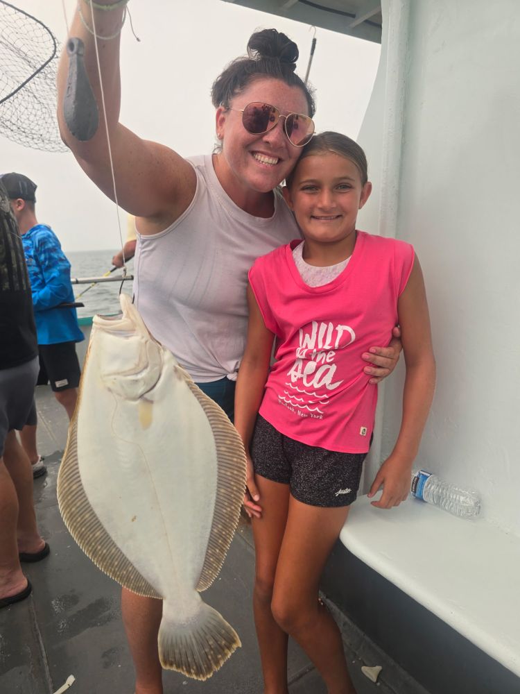 Woman and girl smile, holding a large flatfish on a boat.