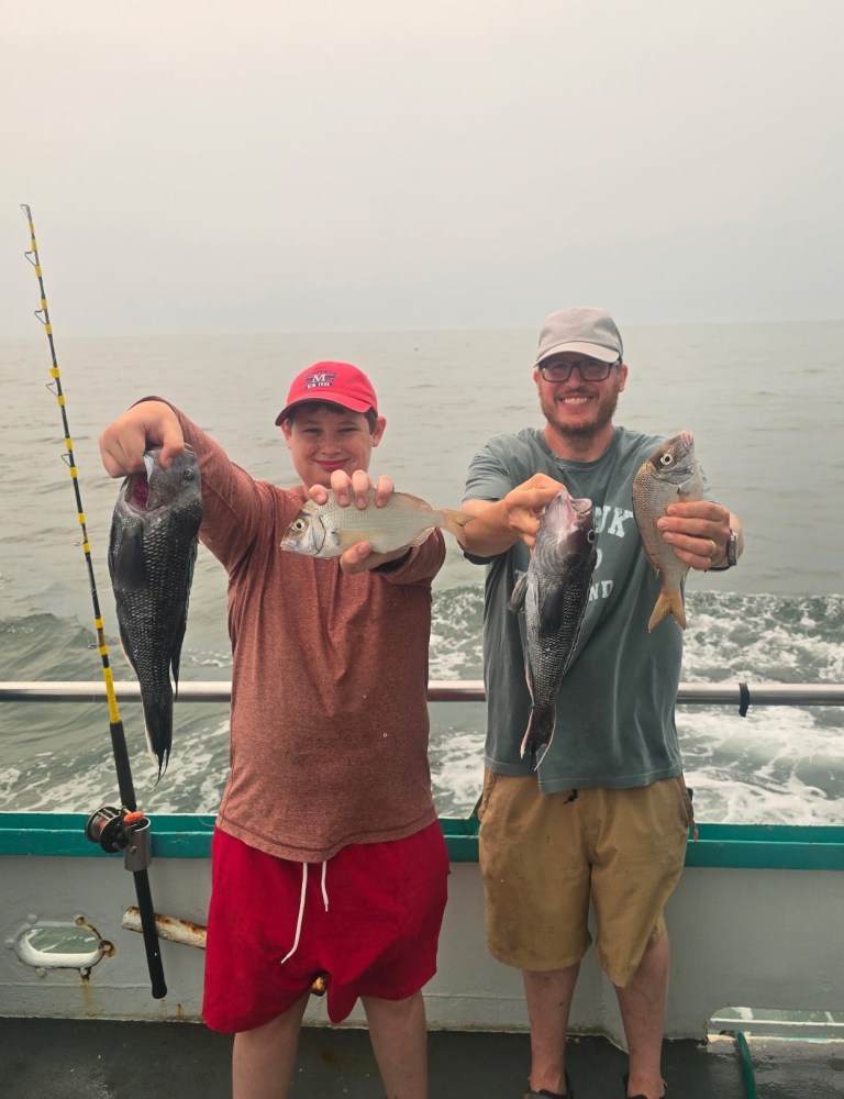 Two people holding fish on a boat with ocean backdrop.