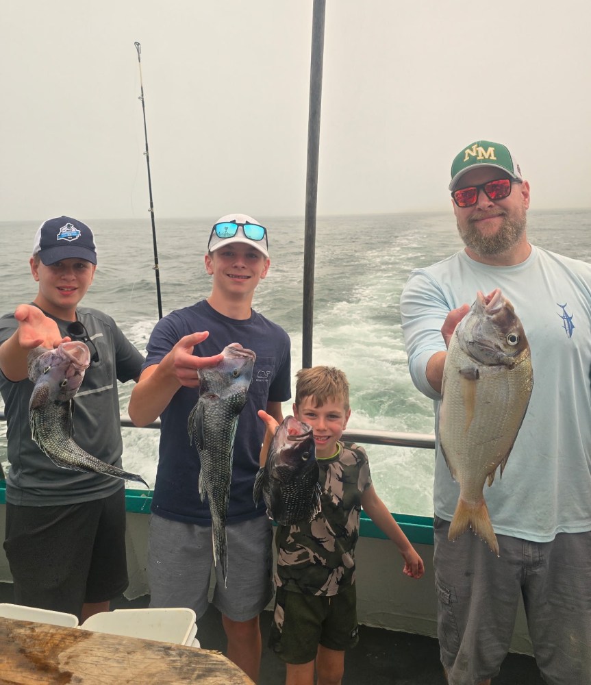 Four people on a boat holding fish, smiling at the camera.