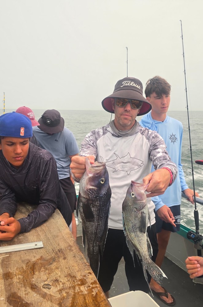 Group of people on a boat, one holding two fish.