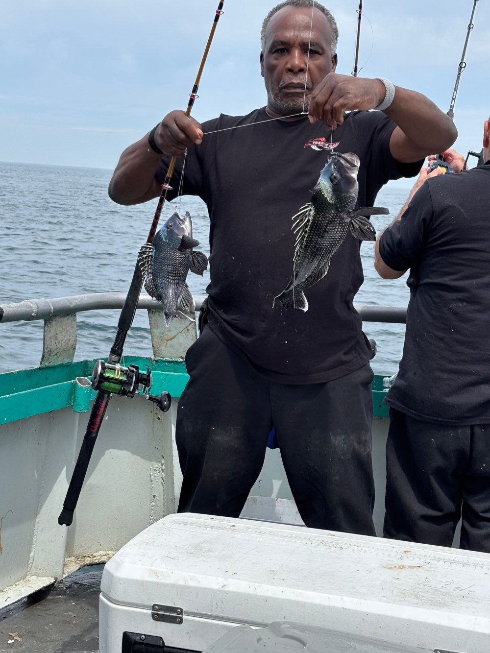 Man on boat holding two fish on fishing lines.