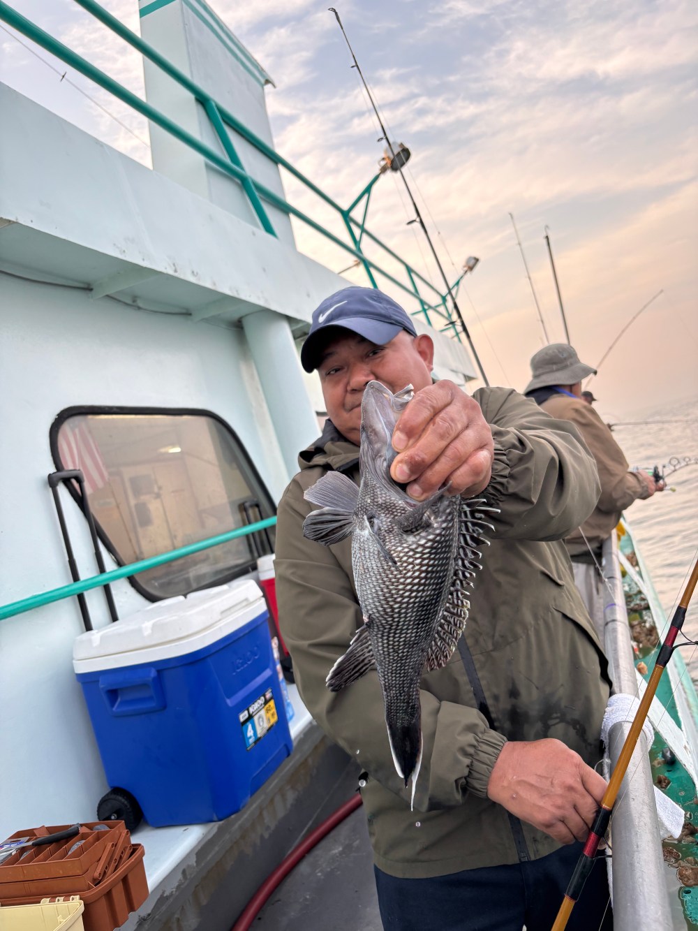 Person holding a fish on a boat, with fishing rods and coolers visible.