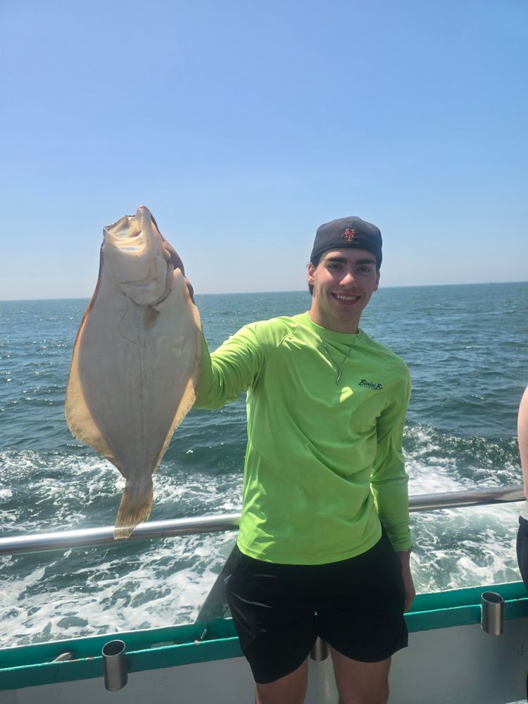 Person holding a large flatfish on a boat with ocean backdrop.