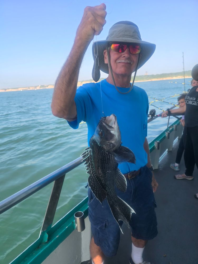 Man on boat holding a fish, wearing a blue shirt and hat.