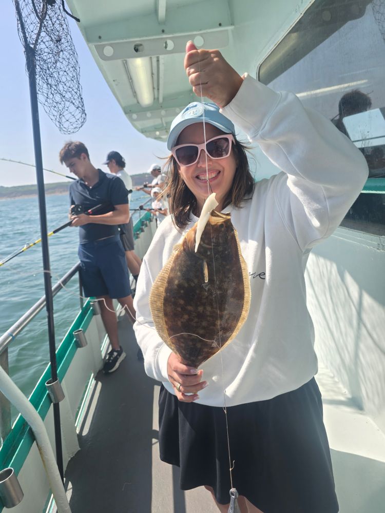 Person holding a flatfish on a boat, smiling with others fishing nearby.