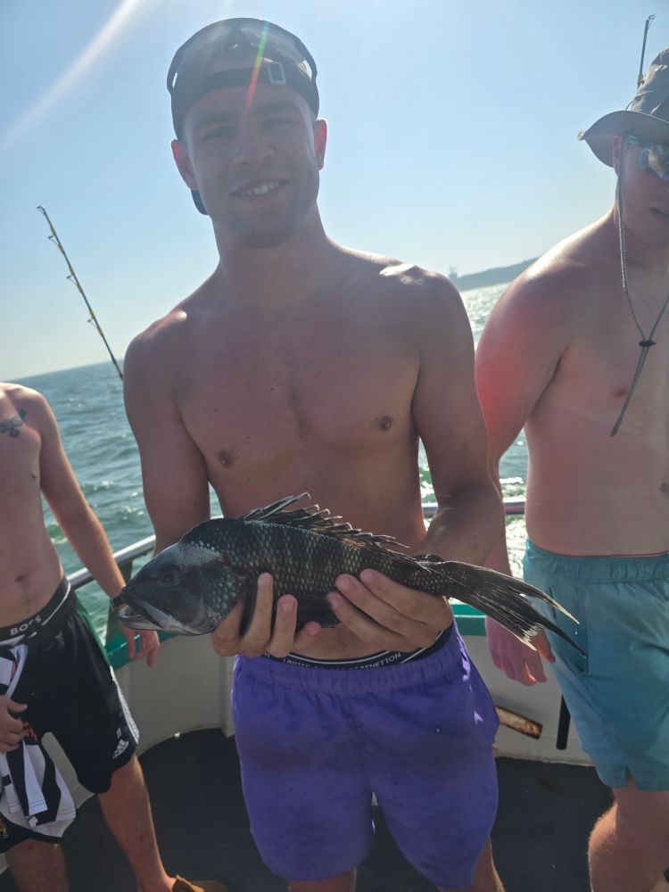 Man on a boat holding a fish, with others in the background, sunny day.