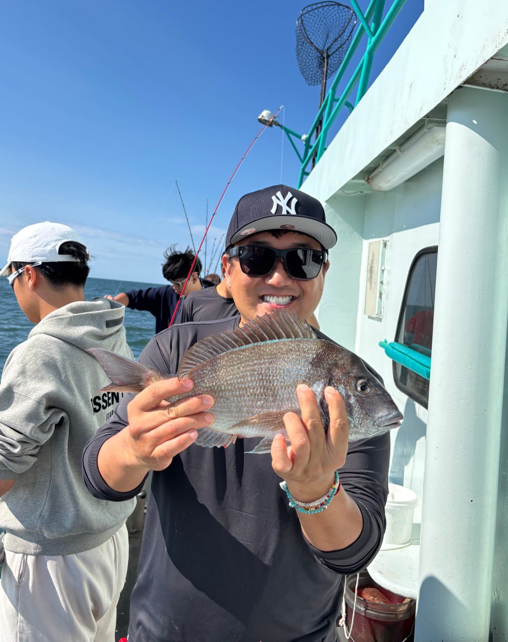 Man in sunglasses holding fish on a boat with others fishing.