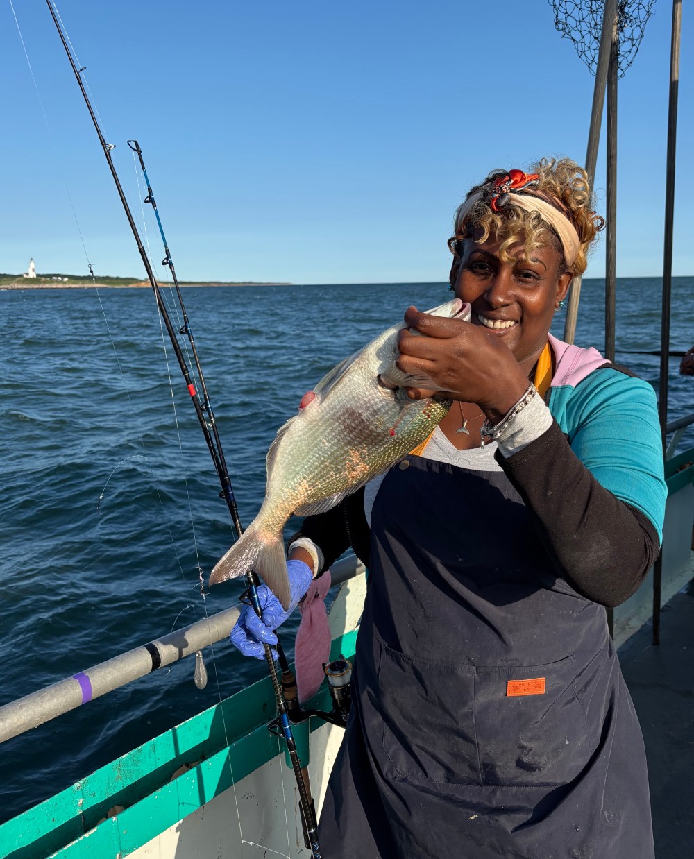 Person smiling with fish on a boat against the ocean backdrop.