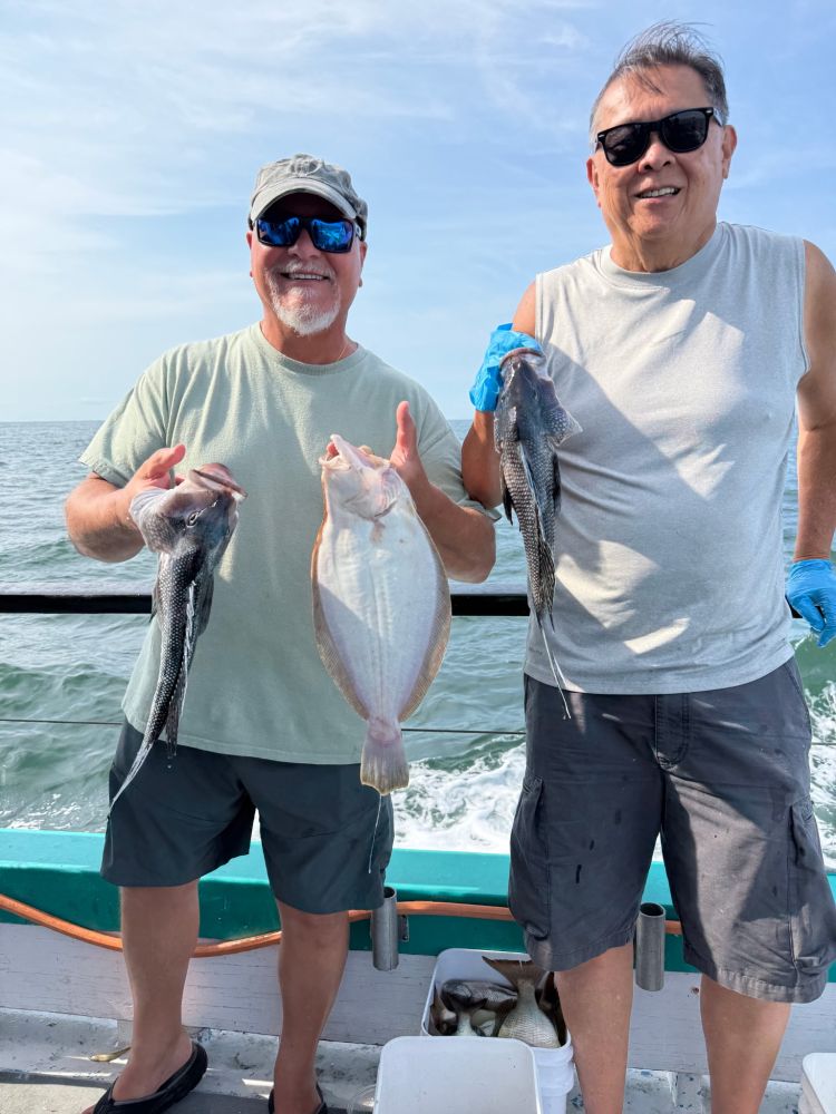 Two men on a boat holding caught fish, smiling at the camera.