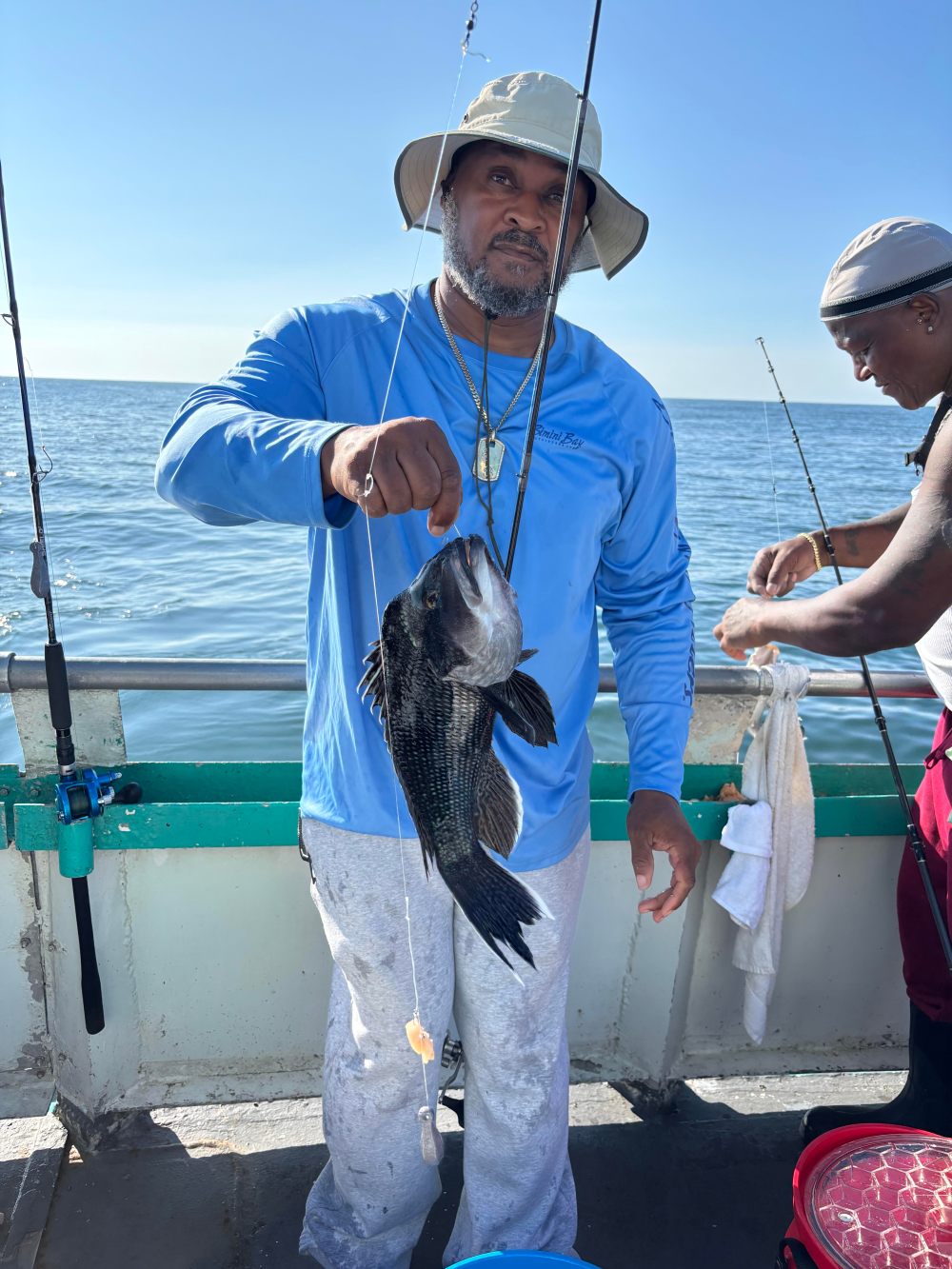 Man on boat holding large fish, another man stands beside him with fishing gear.