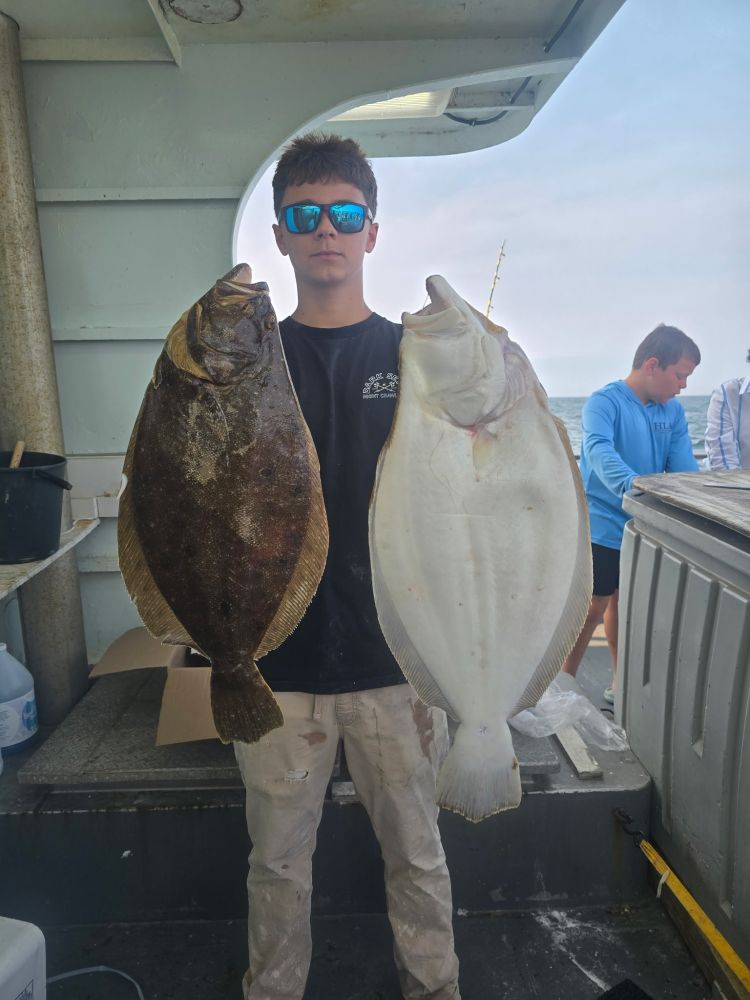 Person holding a large brown fish in one hand and a large white fish in the other, on a boat.