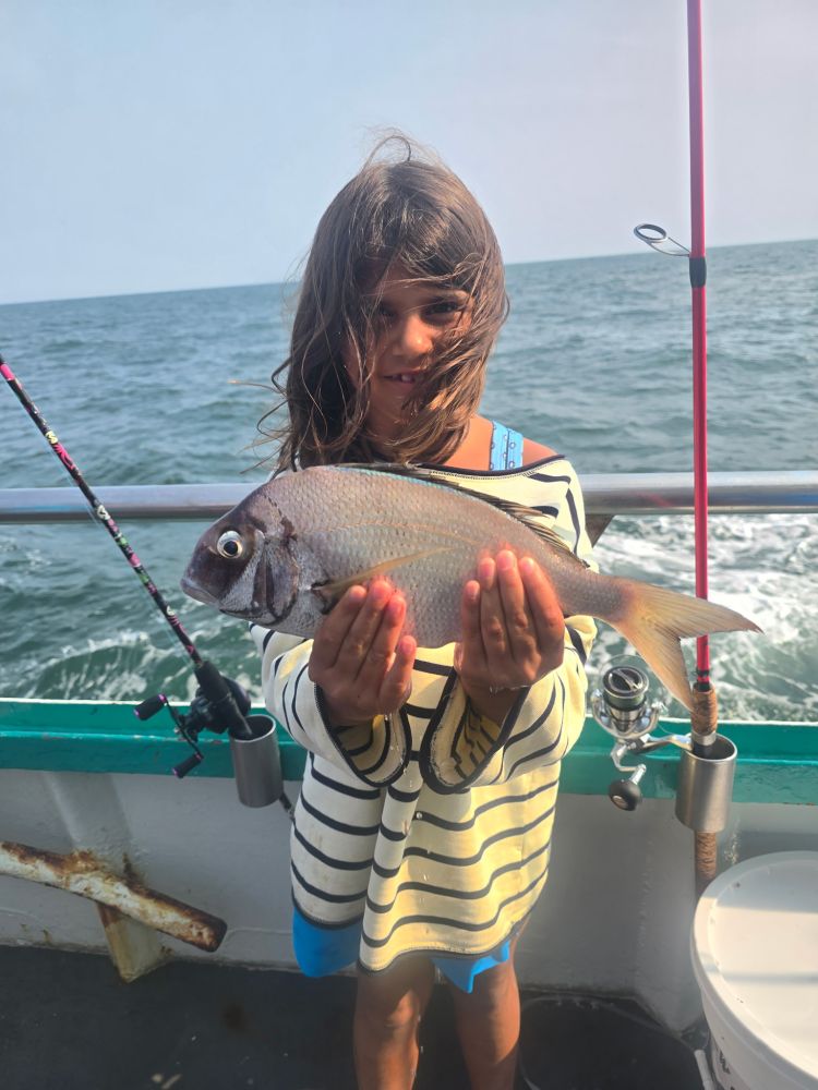 Child on a boat holding a fish, with ocean in the background.