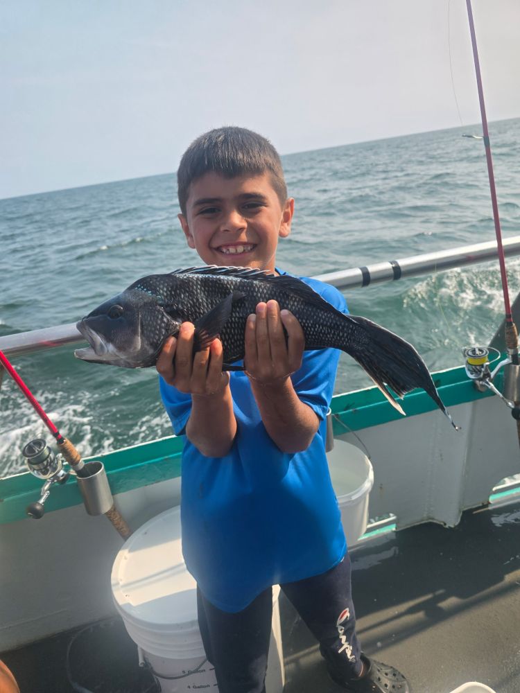 Smiling boy holding a fish on a boat, ocean in the background.