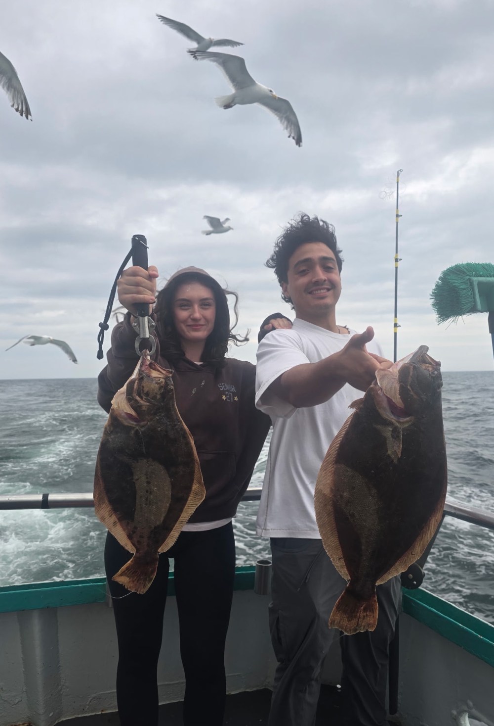 Two people holding fish on a boat with seagulls flying above.