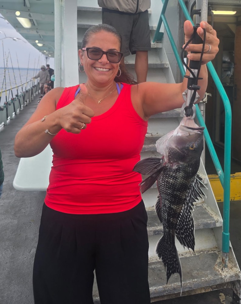 Woman in red tank top holds large fish on a boat, giving a thumbs up.