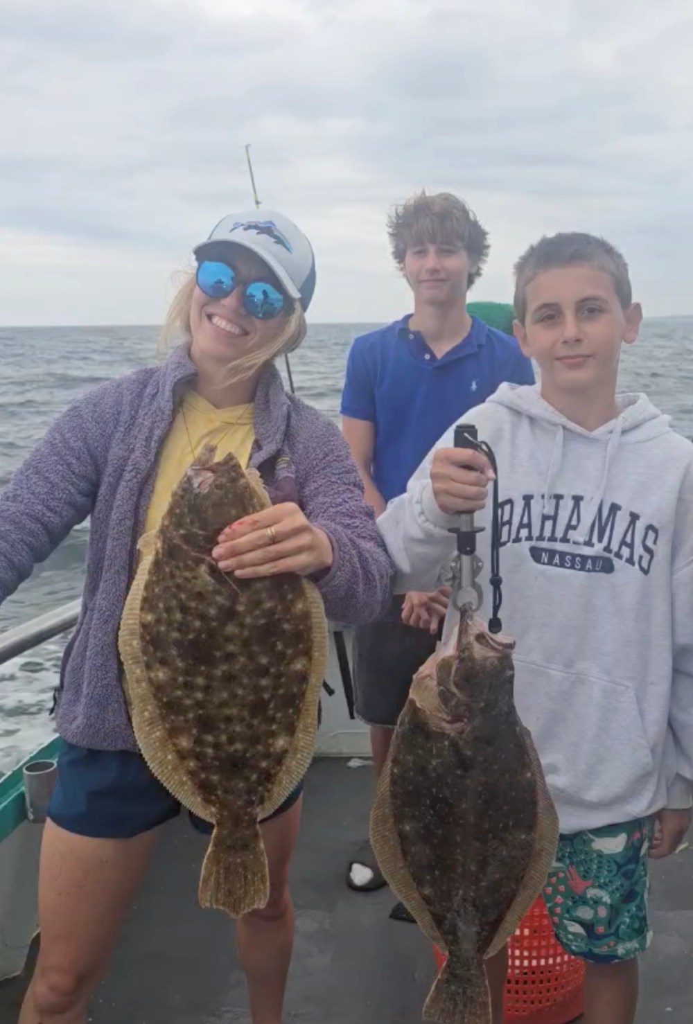 Three people on a boat, two holding large flat fish.