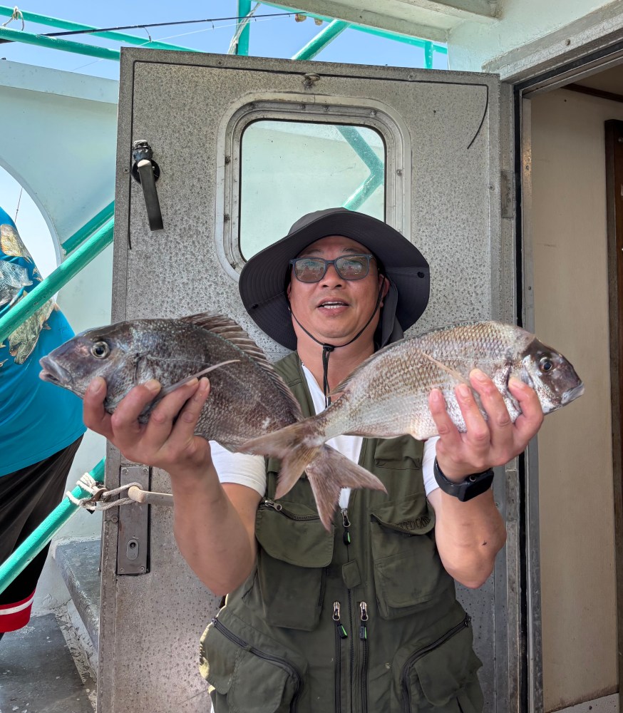 Person holding two fish on a boat, wearing a hat and vest.