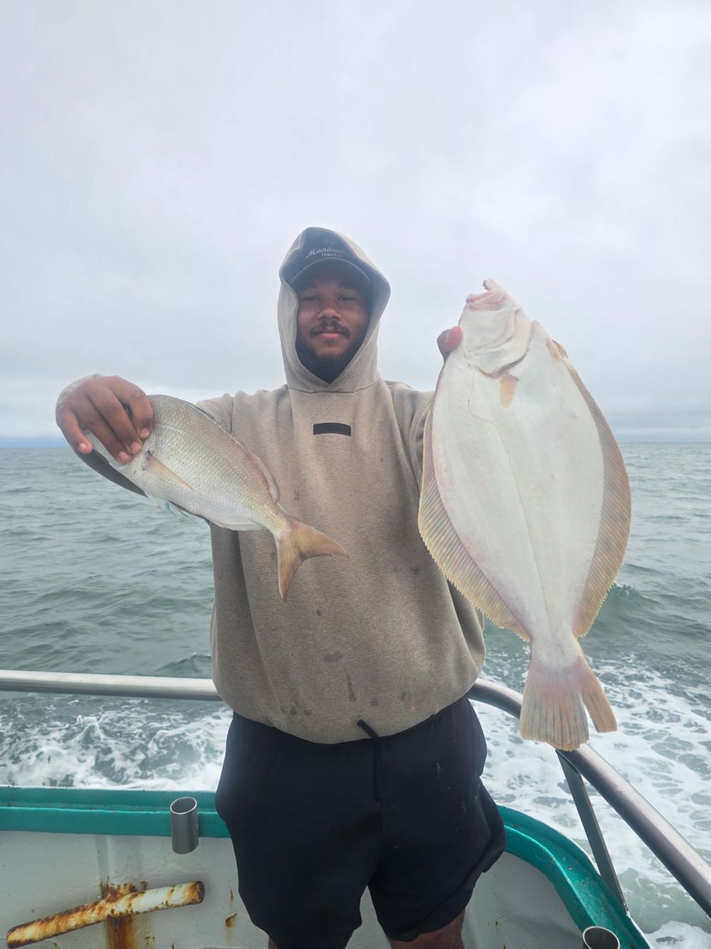 Person holding two fish on a boat in cloudy weather.