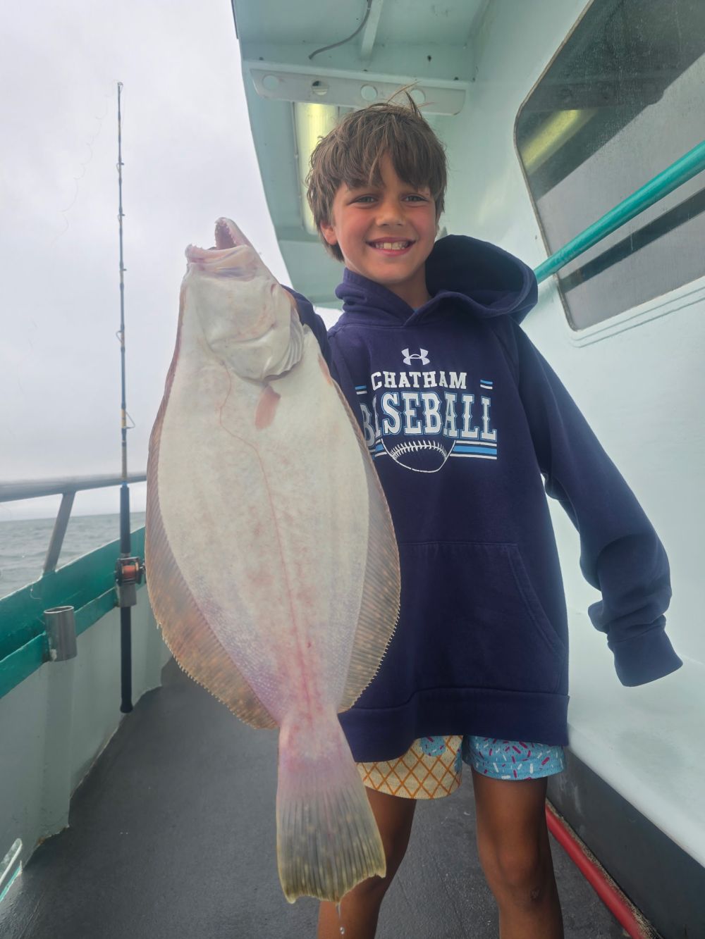 Smiling boy holding a large flatfish on a boat.