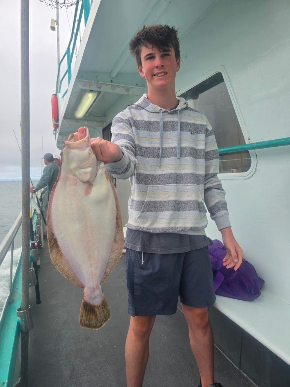 A person on a boat holding a large fish, smiling at the camera.