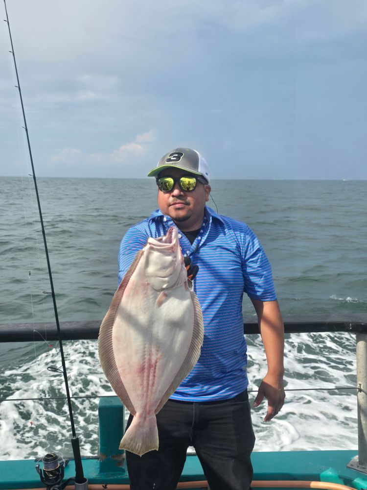 Man holding a large fish on a boat at sea, wearing a blue shirt and cap.