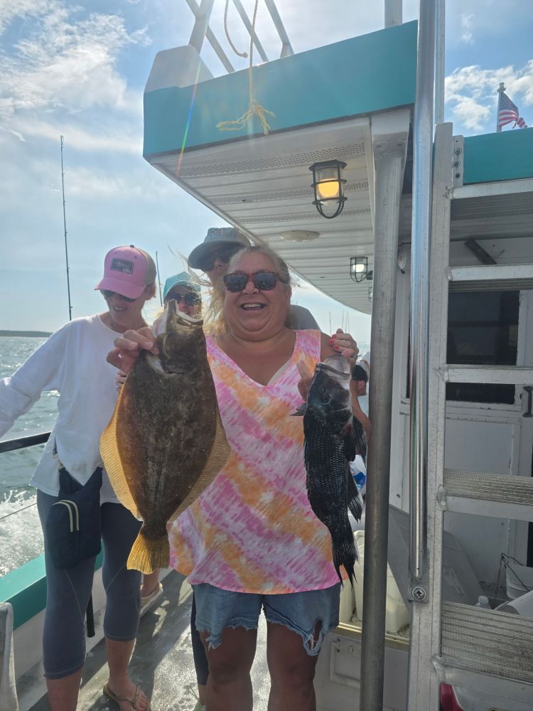 Person on boat holding two large fish, smiling broadly.