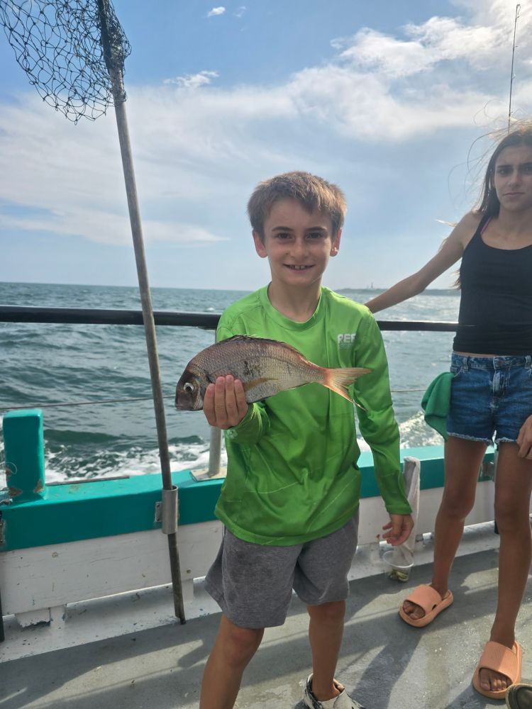 Boy holding a fish on a boat with ocean in the background.