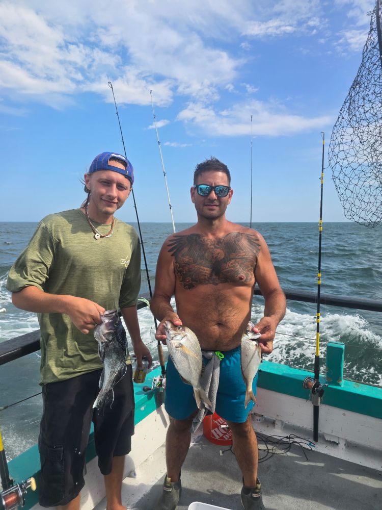 Two people on a boat holding fish with fishing rods in the background.