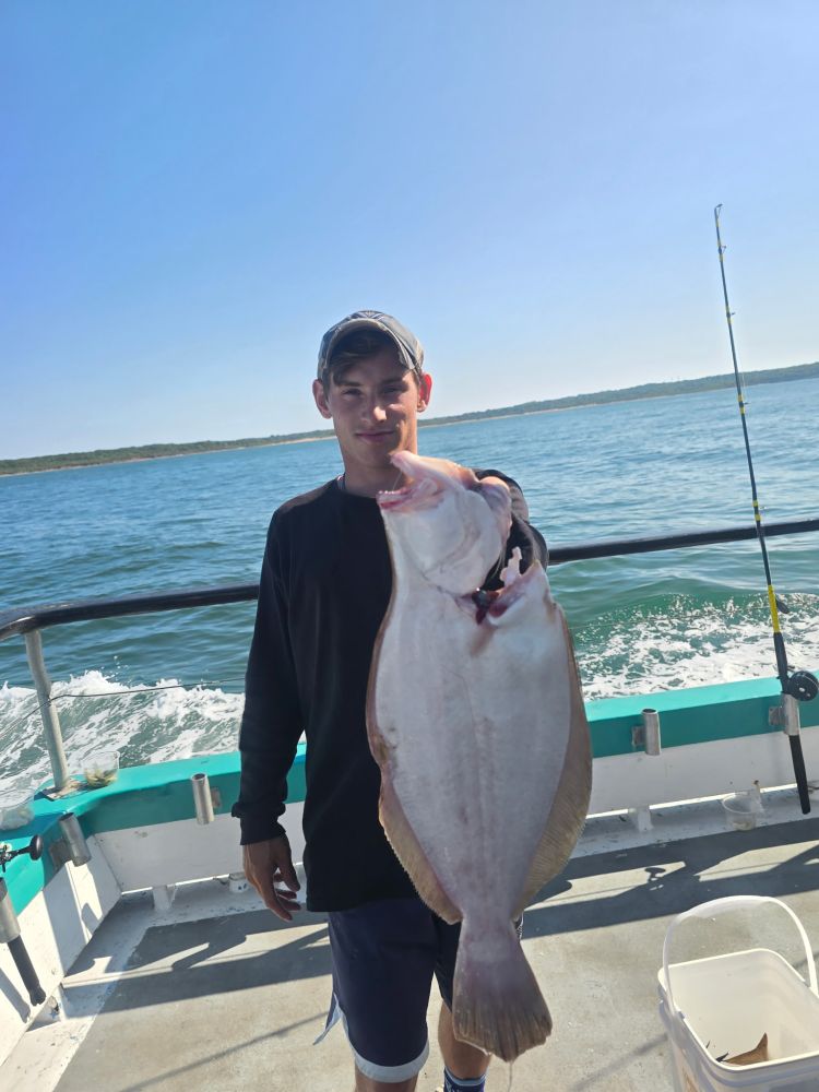 Person holding a large fish on a boat with ocean in the background.