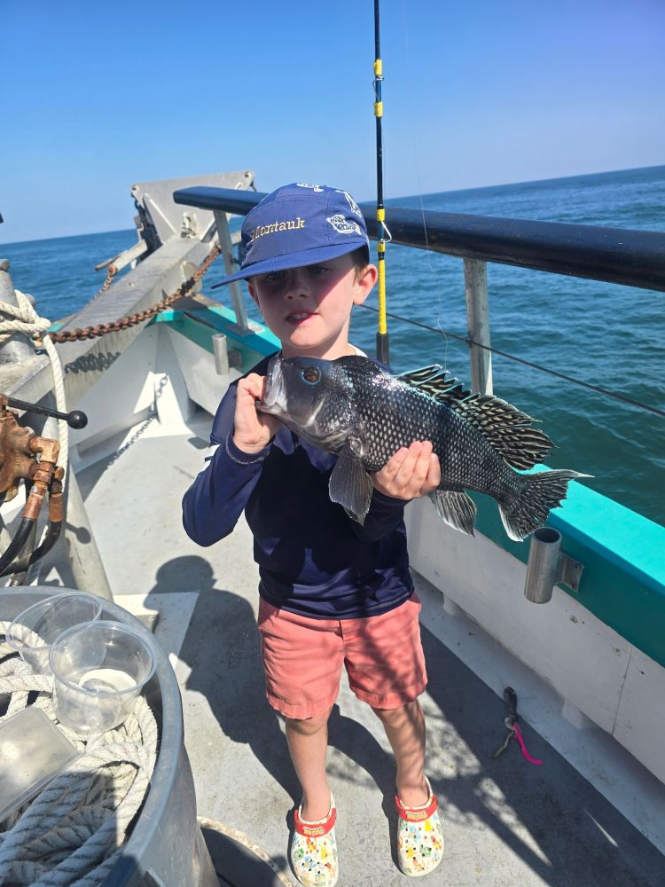 Child on boat holding a large fish, wearing blue hat and shirt.