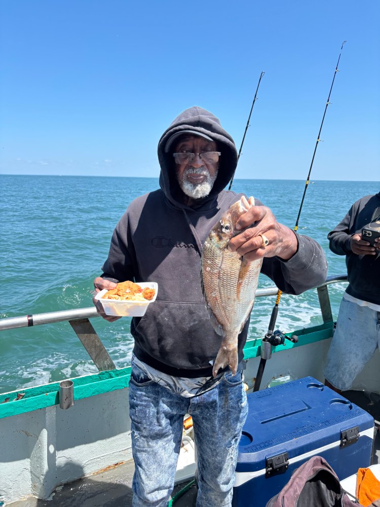 Man on boat holding a fish and food tray, with ocean in background.