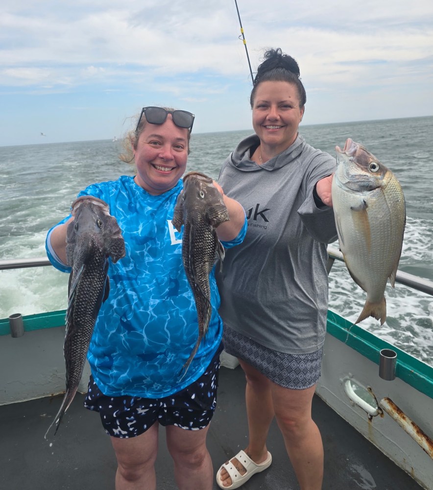 Two women on a boat hold freshly caught fish, smiling at the camera.